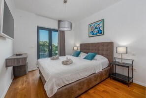A bedroom with a large bed, two bedside tables, a ceiling light, a painting, and a view of greenery through a window. - Villa Coratina ZadarVillas (Lun)