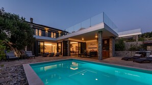Une maison moderne dotée d’une piscine, d’un espace salon extérieur et d’un mur en pierre.