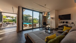 Un salon moderne avec un grand canapé, un téléviseur et une vue sur une piscine.
