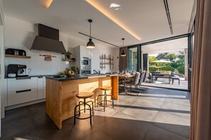 A modern kitchen with a wooden island, bar stools, a built-in oven, and a large window overlooking a garden. - Villa Coratina ZadarVillas (Lun)