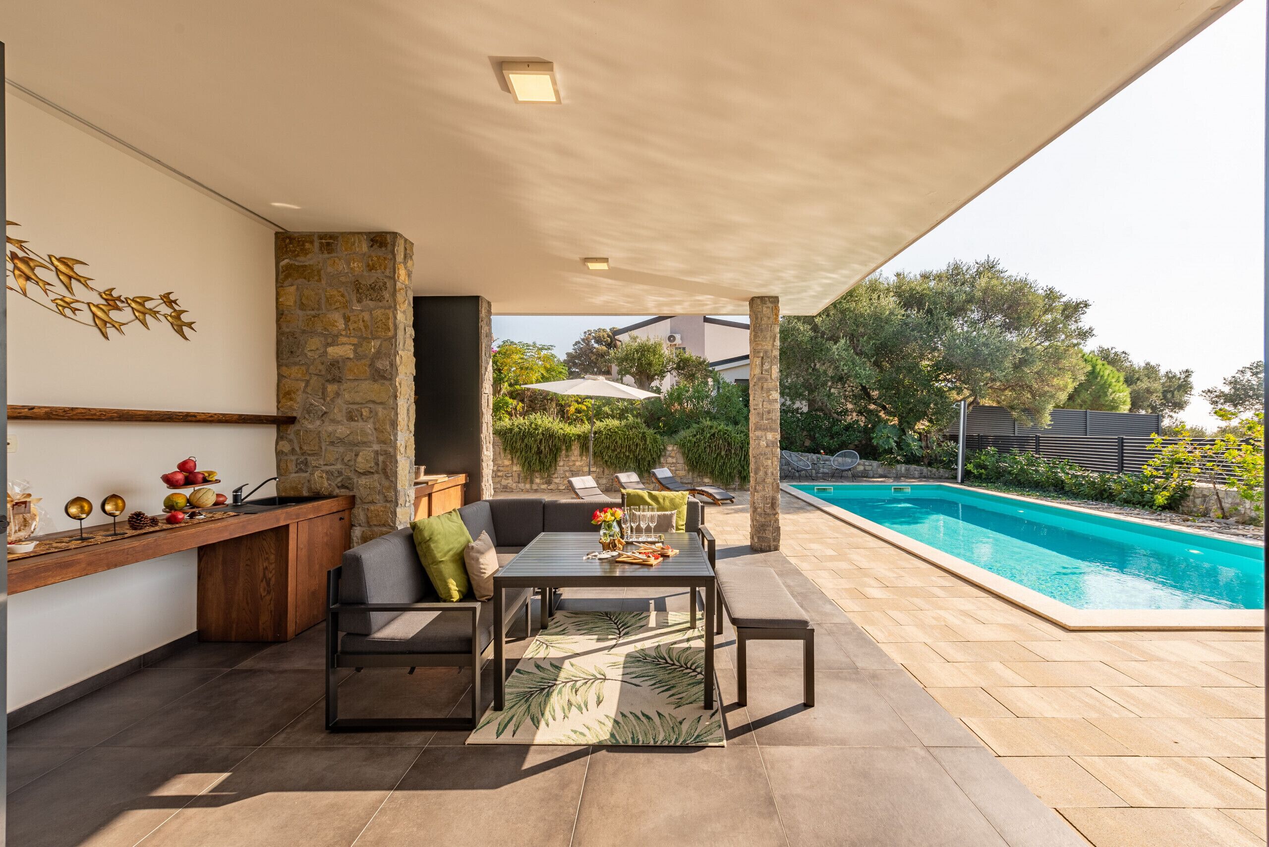 A covered outdoor area with a pool, stone wall, and seating.