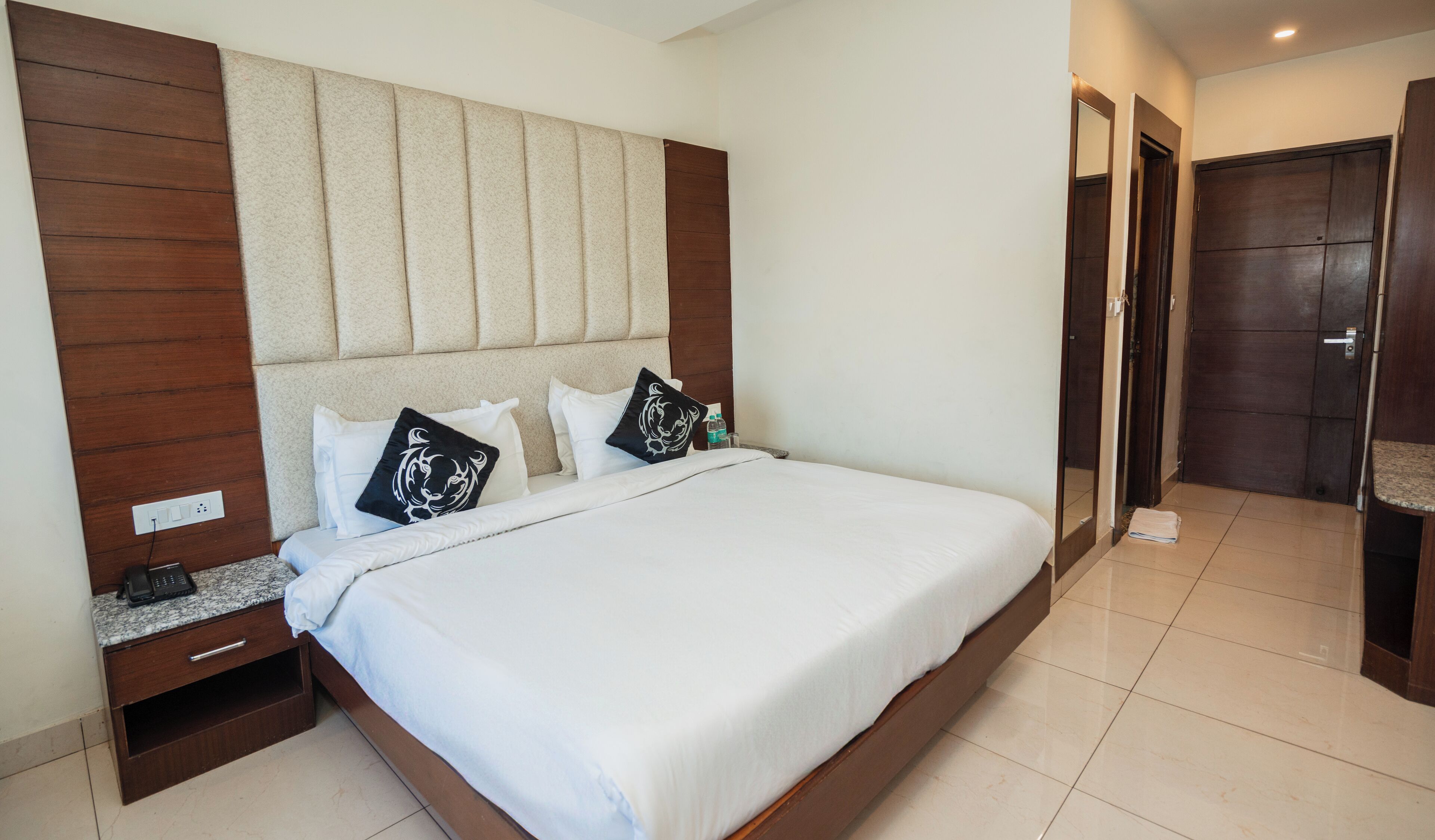 Una camera d'albergo con un letto grande, una testiera in legno, un comodino e un bagno visibile attraverso una porta aperta.