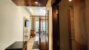 A hallway with a wooden floor, a black table, a wooden door, and a view to a balcony with a table and chairs. - Trideus Chandseena Valley Resort (Dehradun)