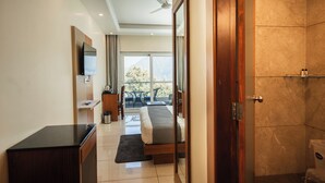 A hotel room with a bed, a desk, a TV, a balcony with a view, and a shower area. - Trideus Chandseena Valley Resort (Dehradun)