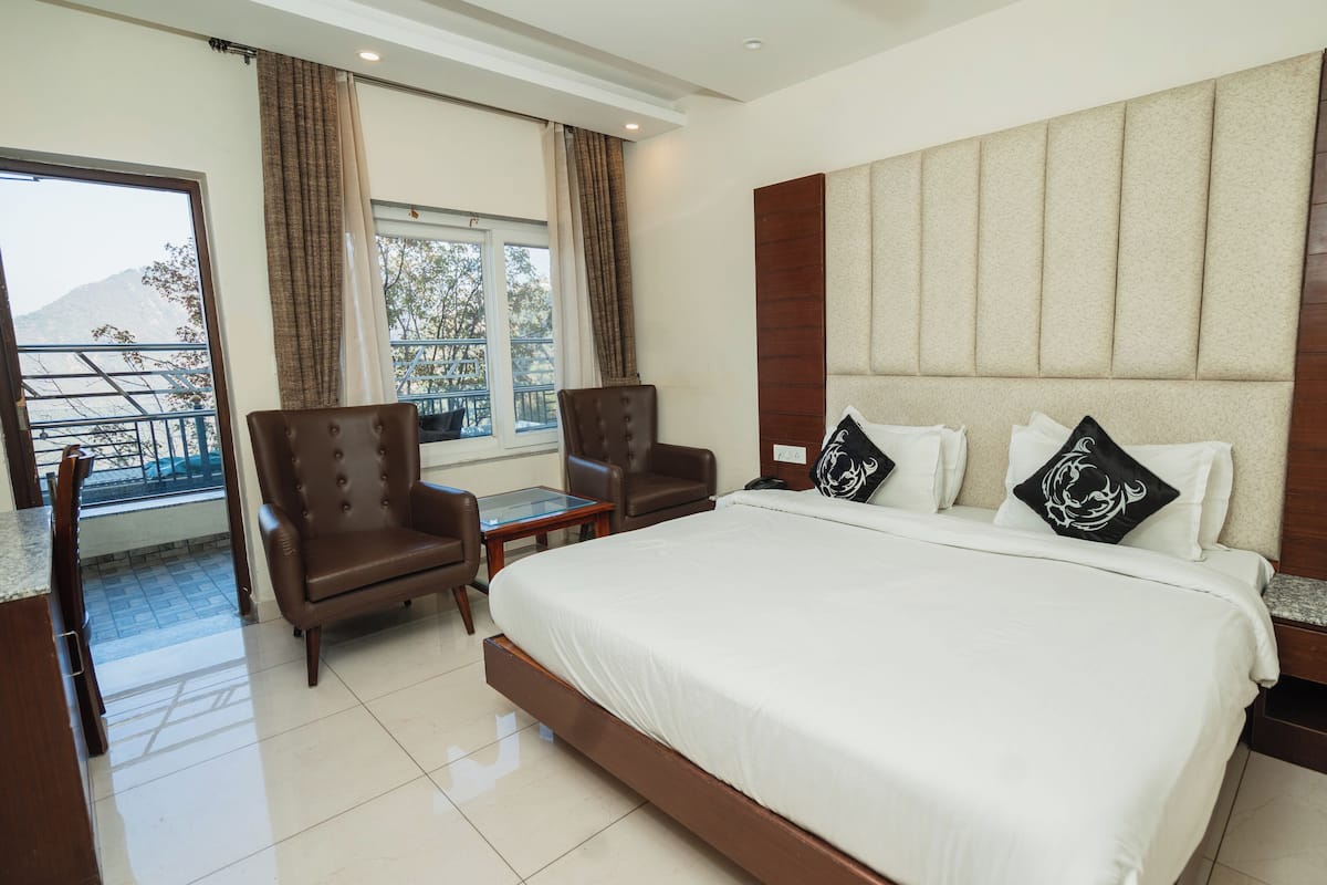 Habitación de hotel con una cama grande, dos sillones, una mesita y vistas a un balcón con una montaña al fondo.