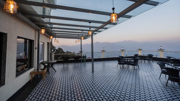 An outdoor terrace with a checkered floor, tables, chairs, and hanging lanterns. - Trideus Chandseena Valley Resort (Dehradun)