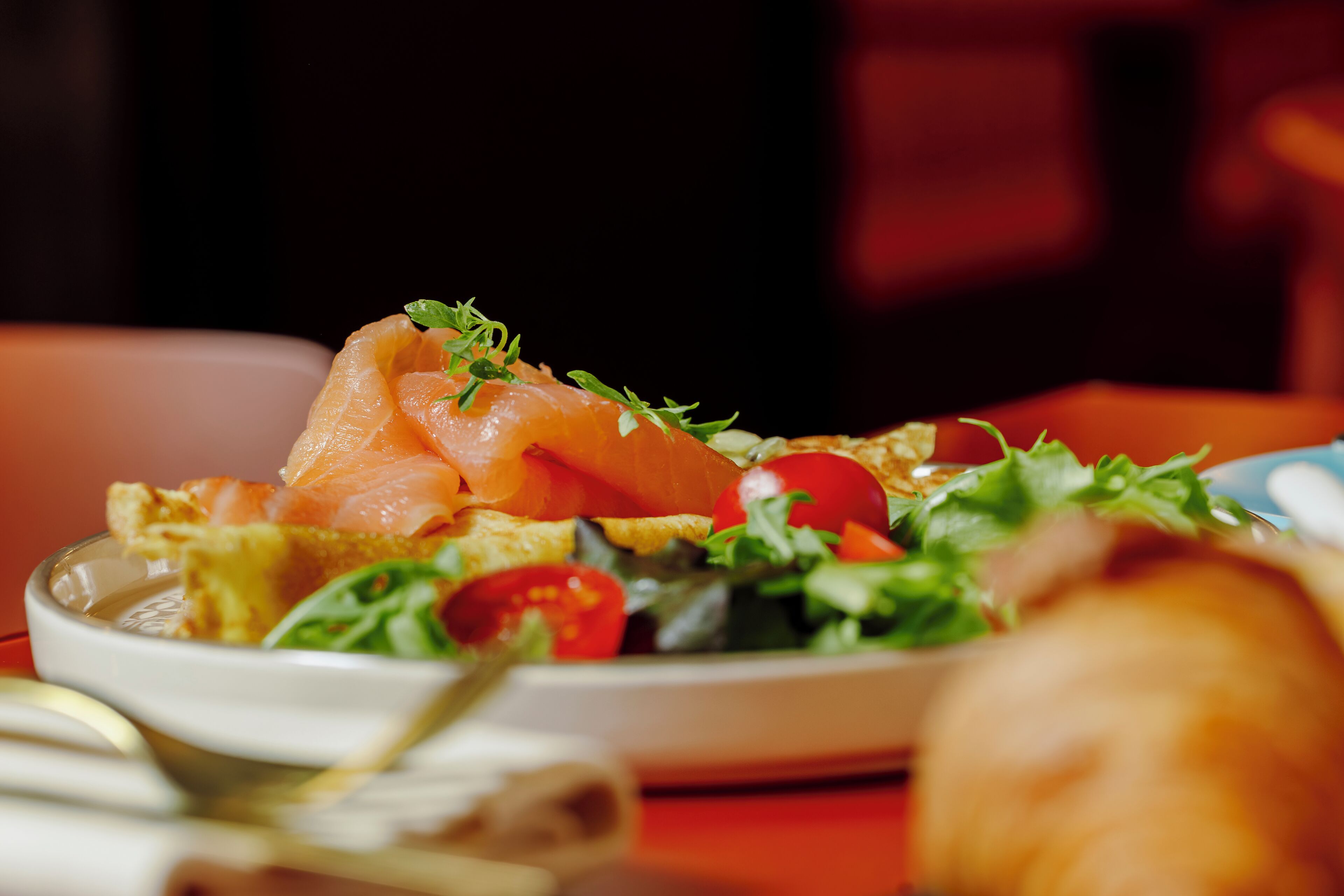A plate of food with smoked salmon, tomatoes, and greens.