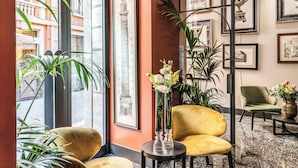 A lobby with a large window, a yellow armchair, a black side table, and framed artwork on the wall. - Residenza Piranesi Boutique Hotel (Rome)