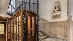 A marble staircase with a wooden elevator and a bust sculpture on the wall. - Residenza Piranesi Boutique Hotel (Rome)
