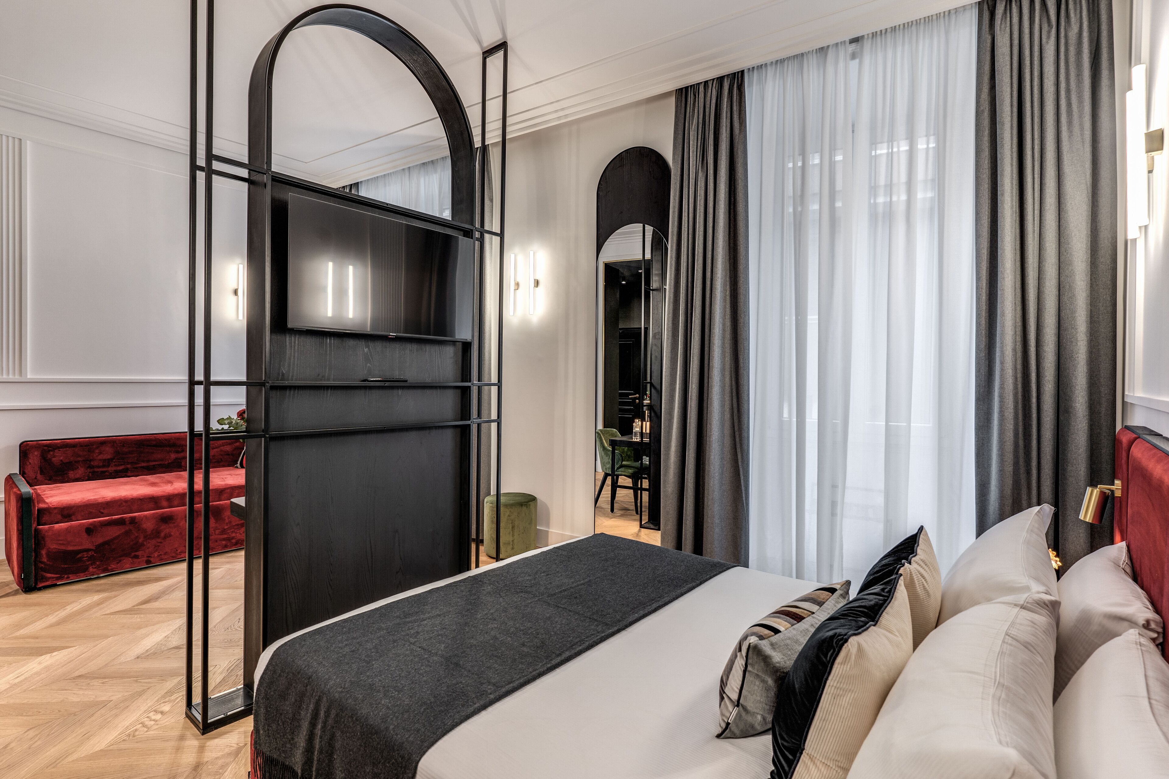 Una habitación de hotel moderna con una cama grande, un sofá rojo, un armario negro y un espejo.