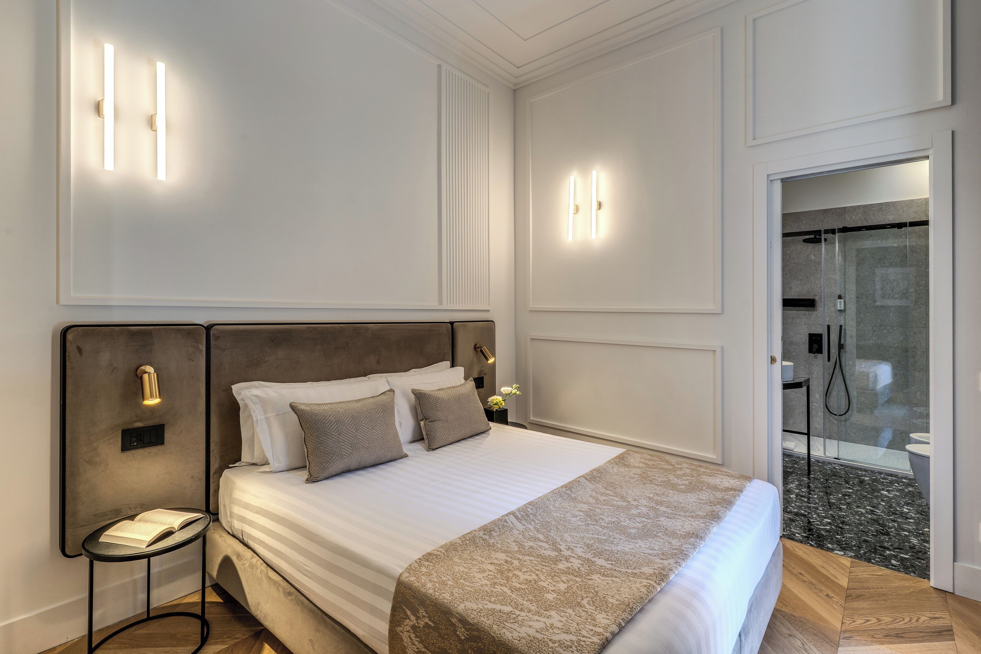Une chambre d’hôtel moderne avec un grand lit, des tables de chevet et un espace douche visible à travers une porte en verre.