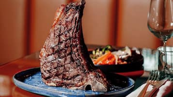 Un plato de carne con un vaso de vino y cubiertos sobre una mesa en un restaurante.