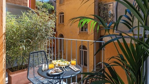 A balcony with a table set for breakfast, including croissants and orange juice, surrounded by plants and a yellow building. - Residenza Piranesi Boutique Hotel (Rome)