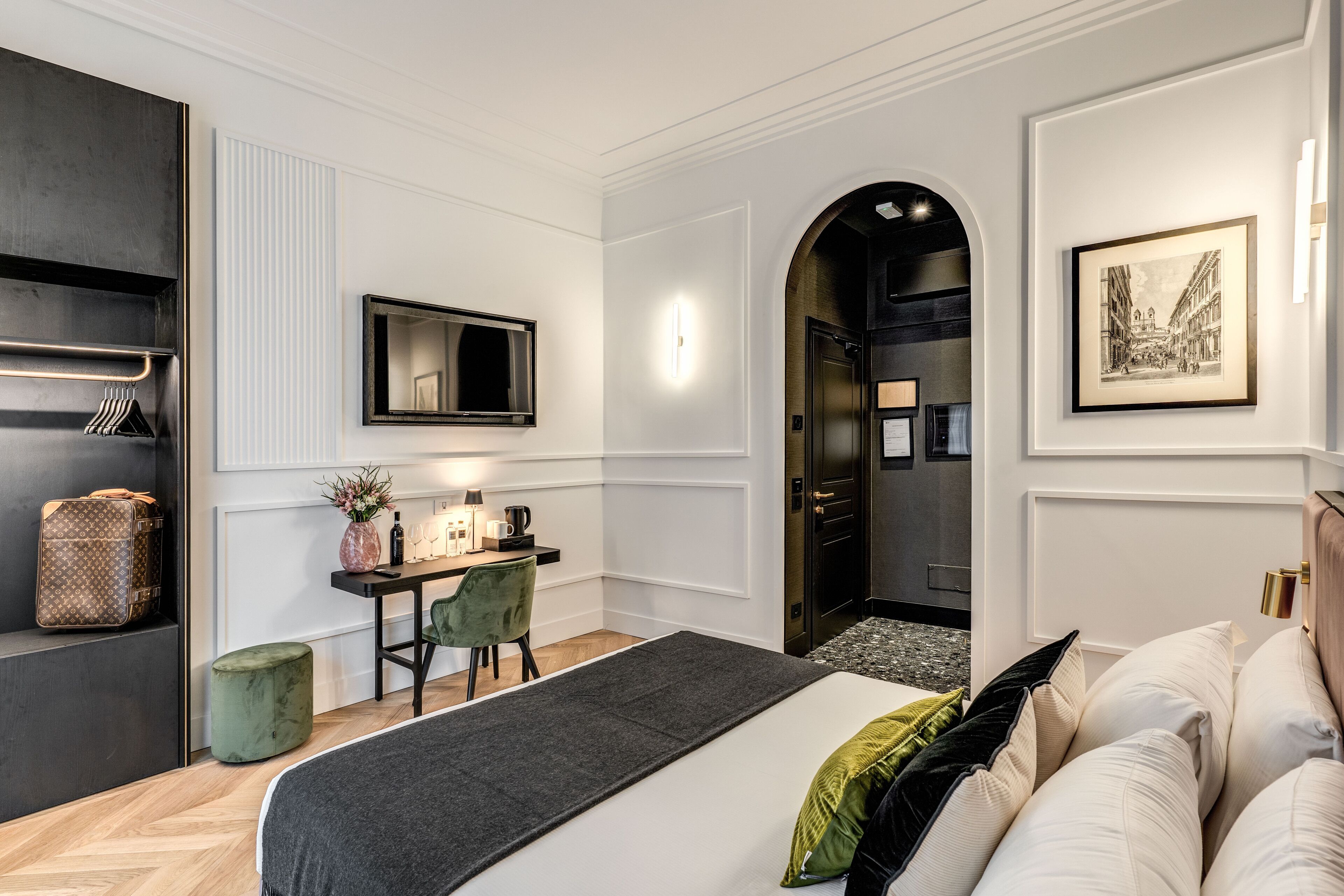 A modern hotel room with a bed, a desk with a chair, a vanity with a mirror, and a framed picture on the wall.