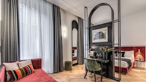 A hotel room with a red sofa, a desk with a chair, a bed with a red headboard, and a large mirror. - Residenza Piranesi Boutique Hotel (Rome)