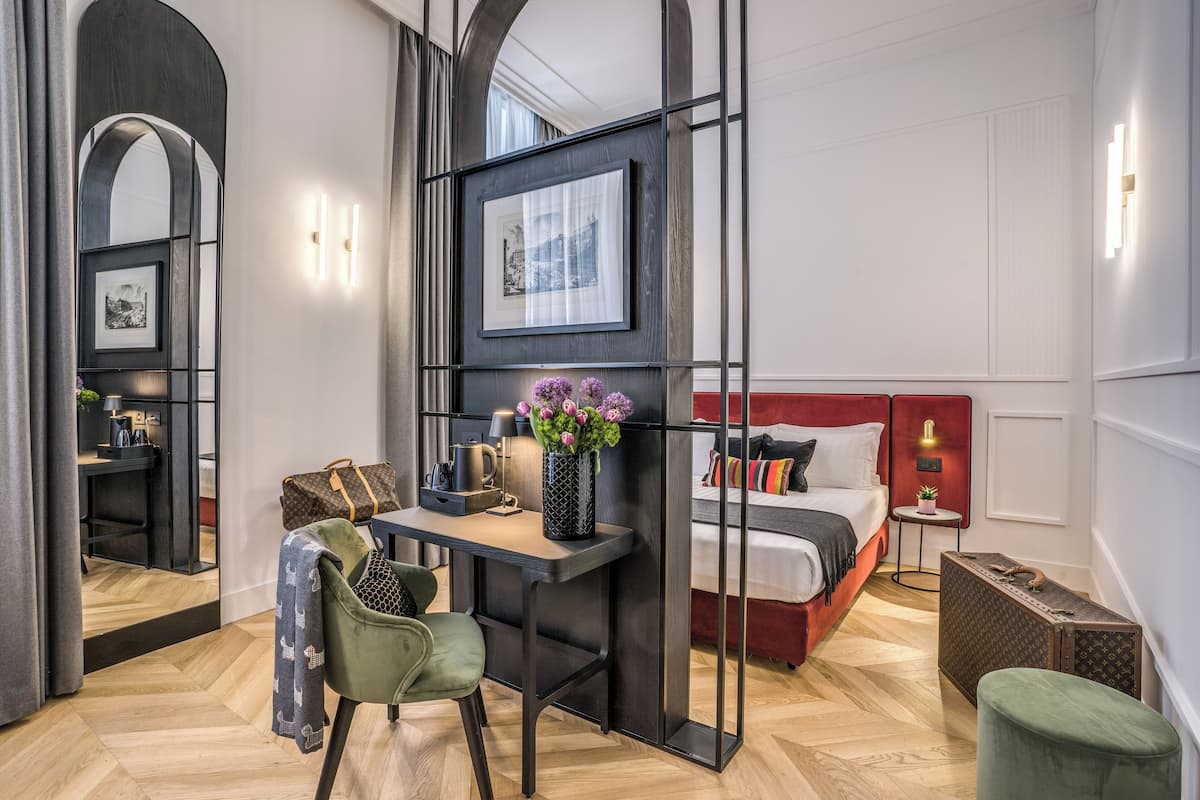 A modern hotel room with a desk, chair, bed, and a large mirror.