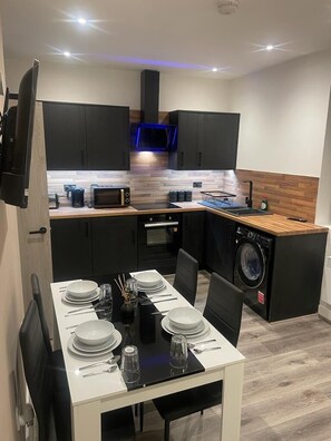 A modern kitchen with black cabinets, a microwave, a built-in oven, and a washing machine. - Boothtown Luxury Apartments (Halifax)
