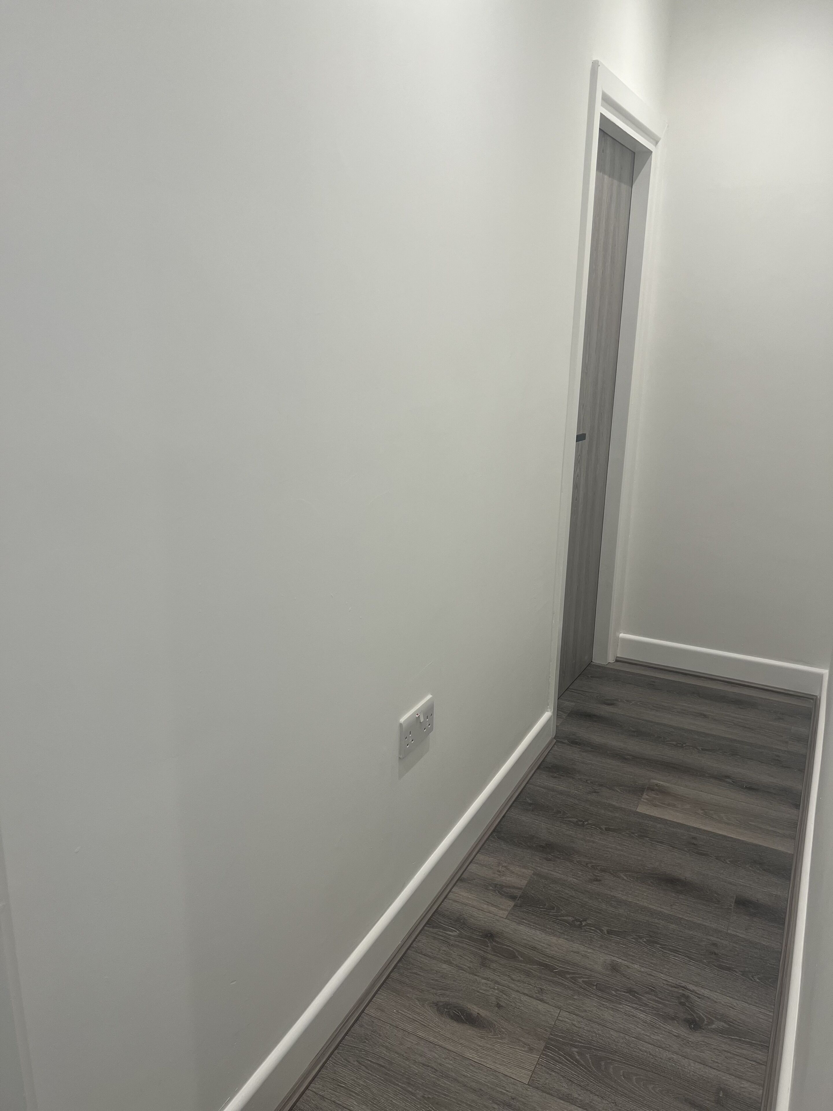 A narrow hallway with a wooden floor and white walls.