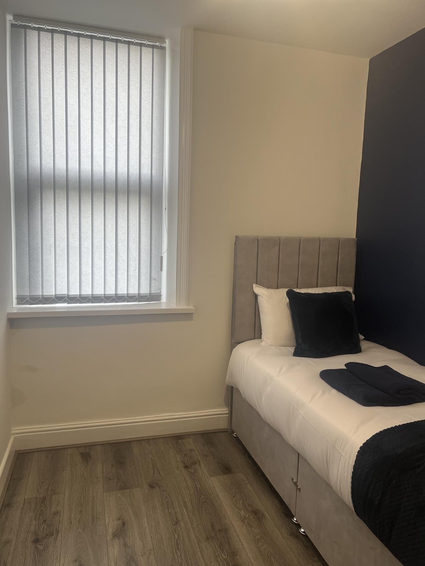 A bedroom with a bed, a window with blinds, and a wooden floor.
