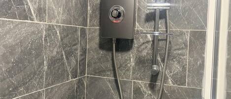 A shower with a handheld showerhead and a control panel mounted on a wall with marble tiles.