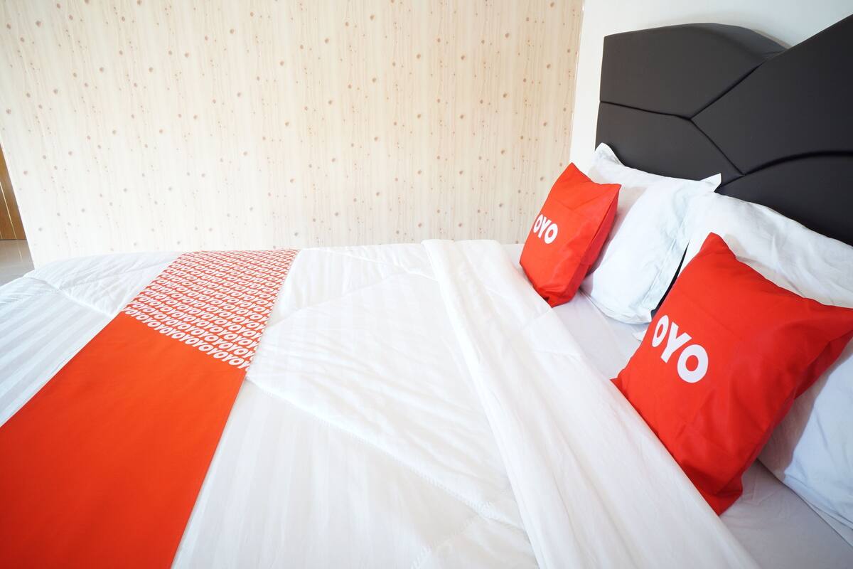 Una habitación de hotel con una cama bien hecha, cabecera y dos almohadas rojas con la palabra "OYO".