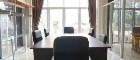 A conference room with a large table and chairs, large windows with curtains, and a view of the outside.