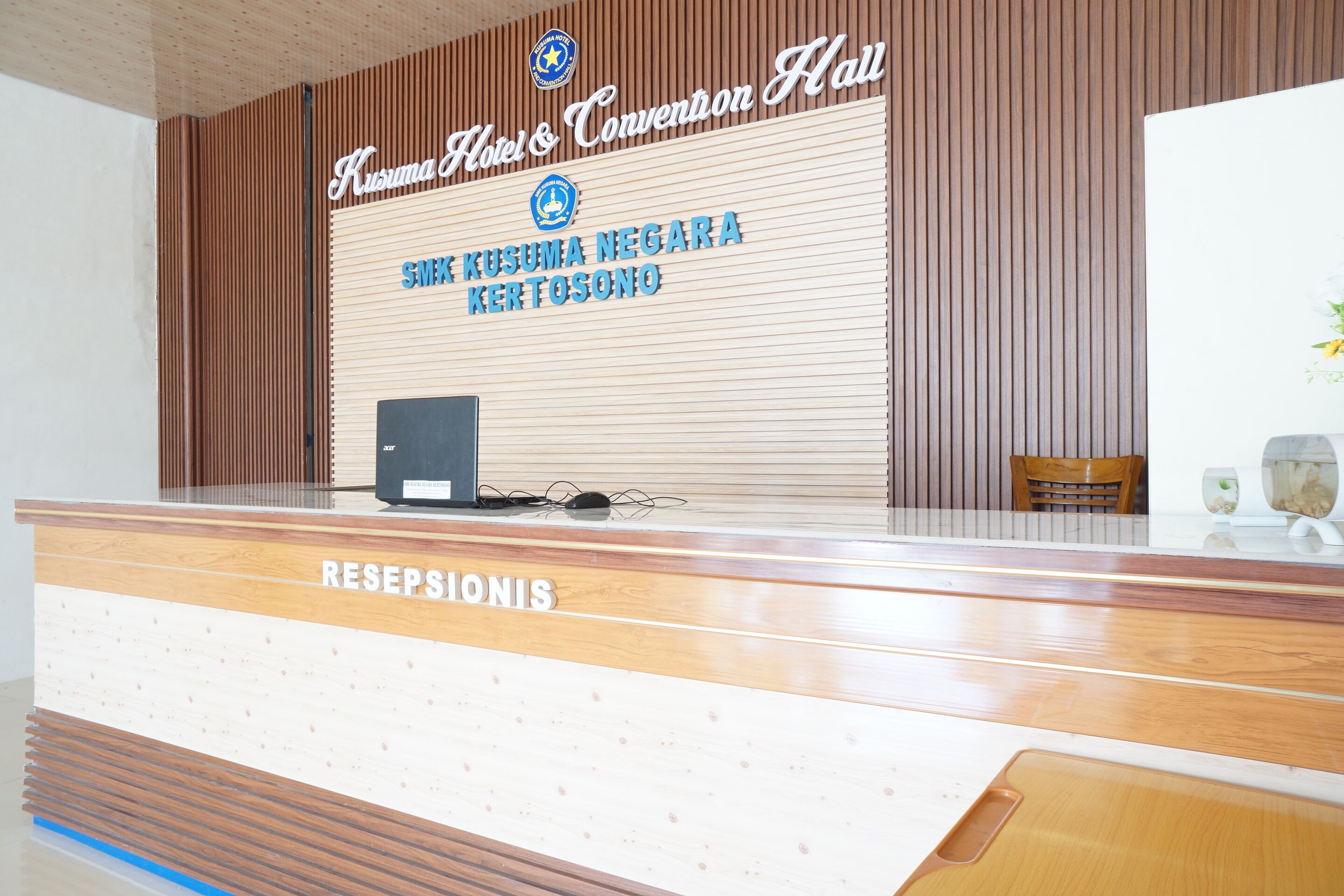 A reception desk with a sign that reads "Hotel & Convention Hall" and "SMK KUSUMA NEGARA KERTOSONO".