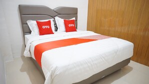 Een net opgemaakt bed met een grijze hoofdbord, wit en rood beddengoed, en twee kussens met de tekst 'OYO'.