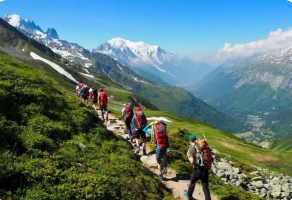 A group of hikers on a mountain trail with snow-capped peaks in the background.