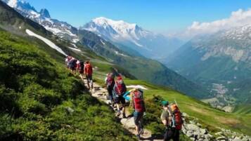 A group of hikers on a mountain trail with snow-capped peaks in the background.