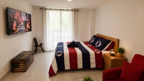 Un dormitorio con cama, un sofá rojo, una mesita con planta, un cofre de madera y un cuadro en la pared.