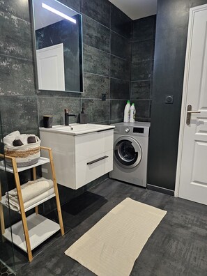 Une salle de bain moderne avec un meuble-lavabo blanc, un lave-linge encastré, un porte-serviettes et un grand miroir.
