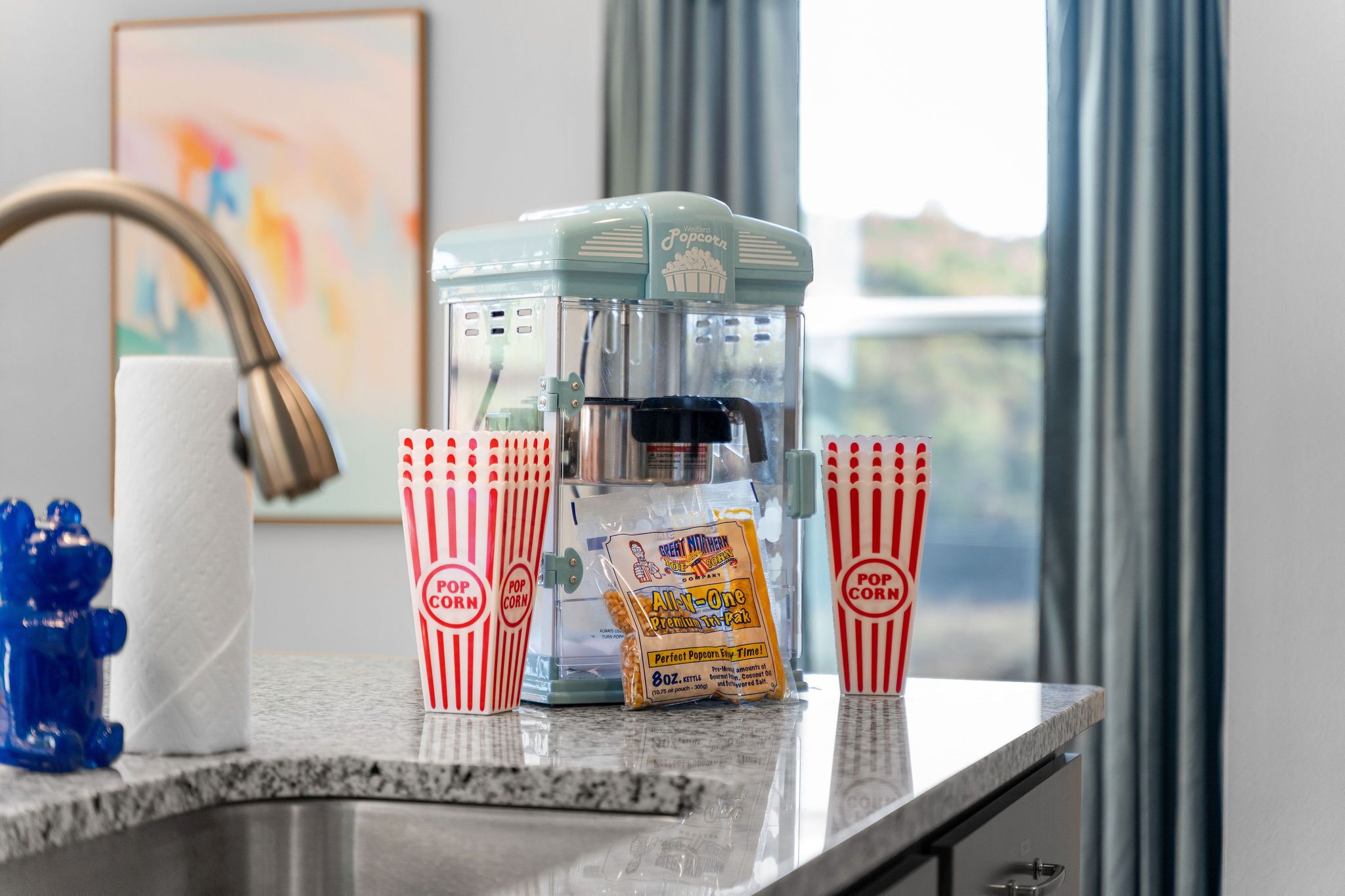 Ein Popcornmacher auf einer Küchenarbeitsplatte mit roten und weißen Streifen-Popcorndosen und einer Tüte Popcorn.