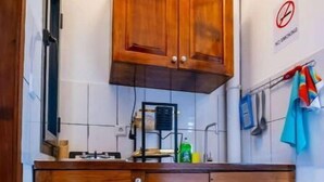 A kitchen with wooden cabinets, a stove, and a trash bin. - Espace Chaleureux , Wifi + Netflix Free, Sécurisé (Douala)