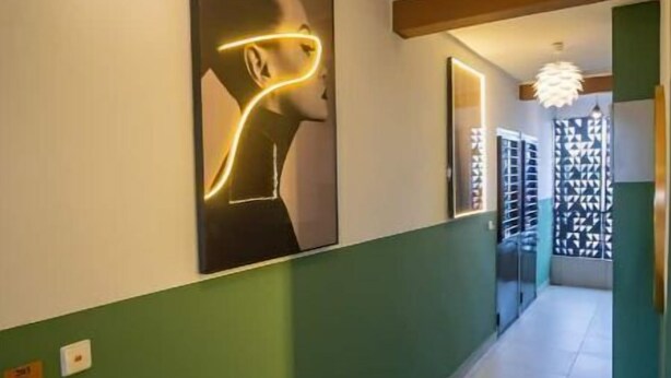 A hallway with a green wall, a framed artwork, a hanging light fixture, and a door leading to a room with patterned curtains. - Espace Chaleureux , Wifi + Netflix Free, Sécurisé (Douala)