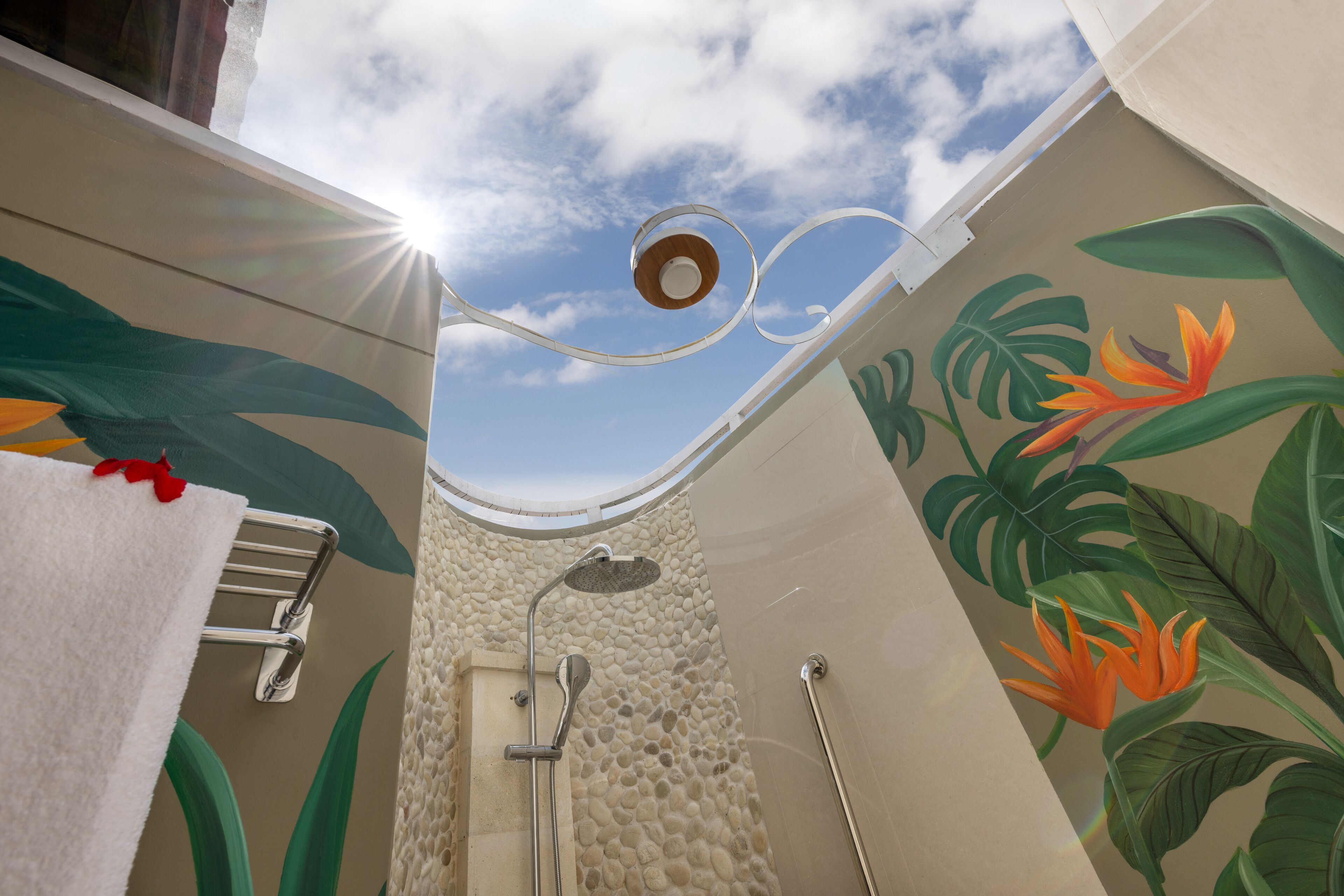 A bathroom with a shower, a towel rack, and a wall mural of tropical leaves and flowers.