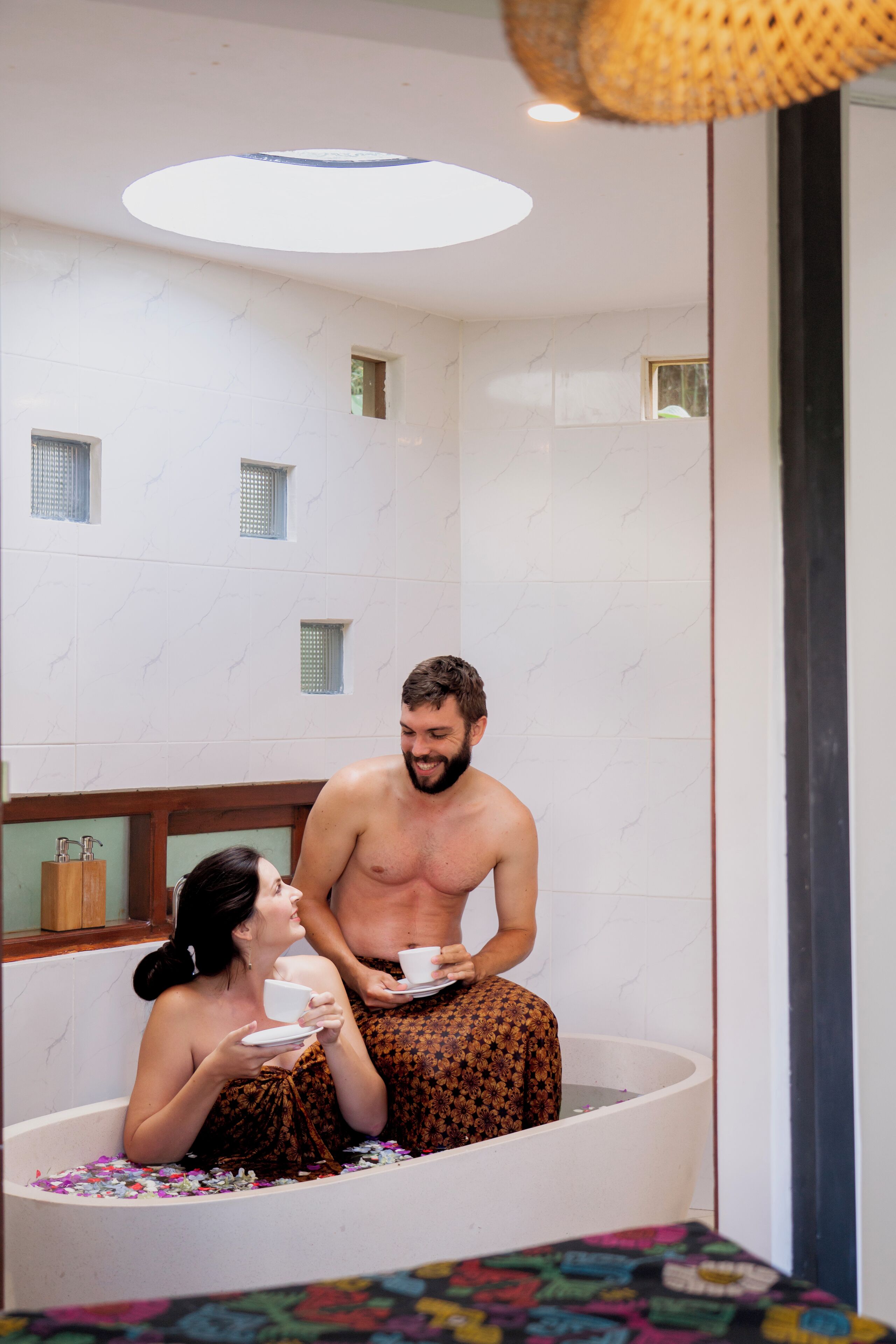 A bathtub with two people, one holding a cup.