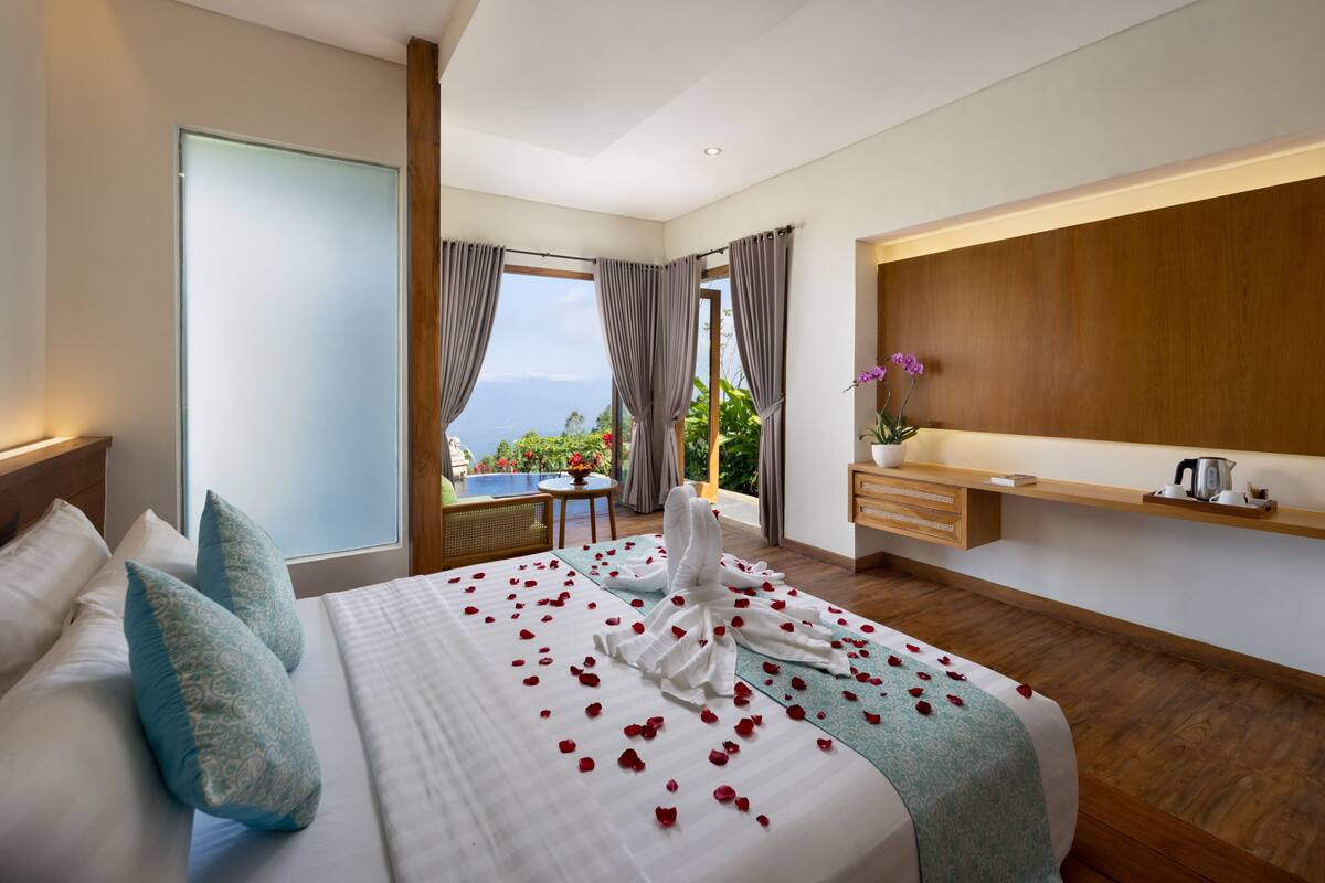 A hotel room with a large bed, a view of the ocean, a small balcony, and a wooden floor.