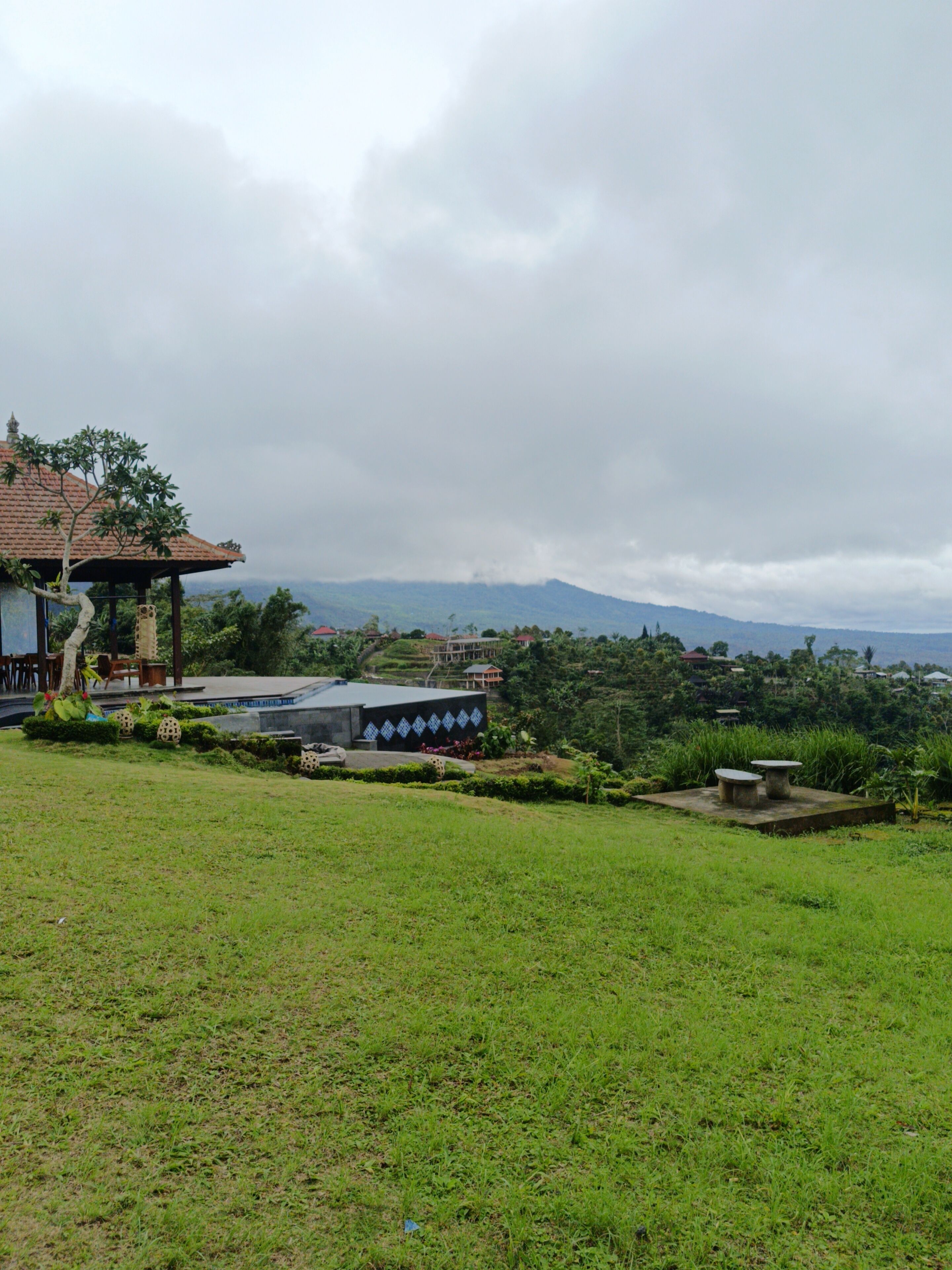 A grassy area with a gazebo, a building with a tiled roof, and a mountain in the background.