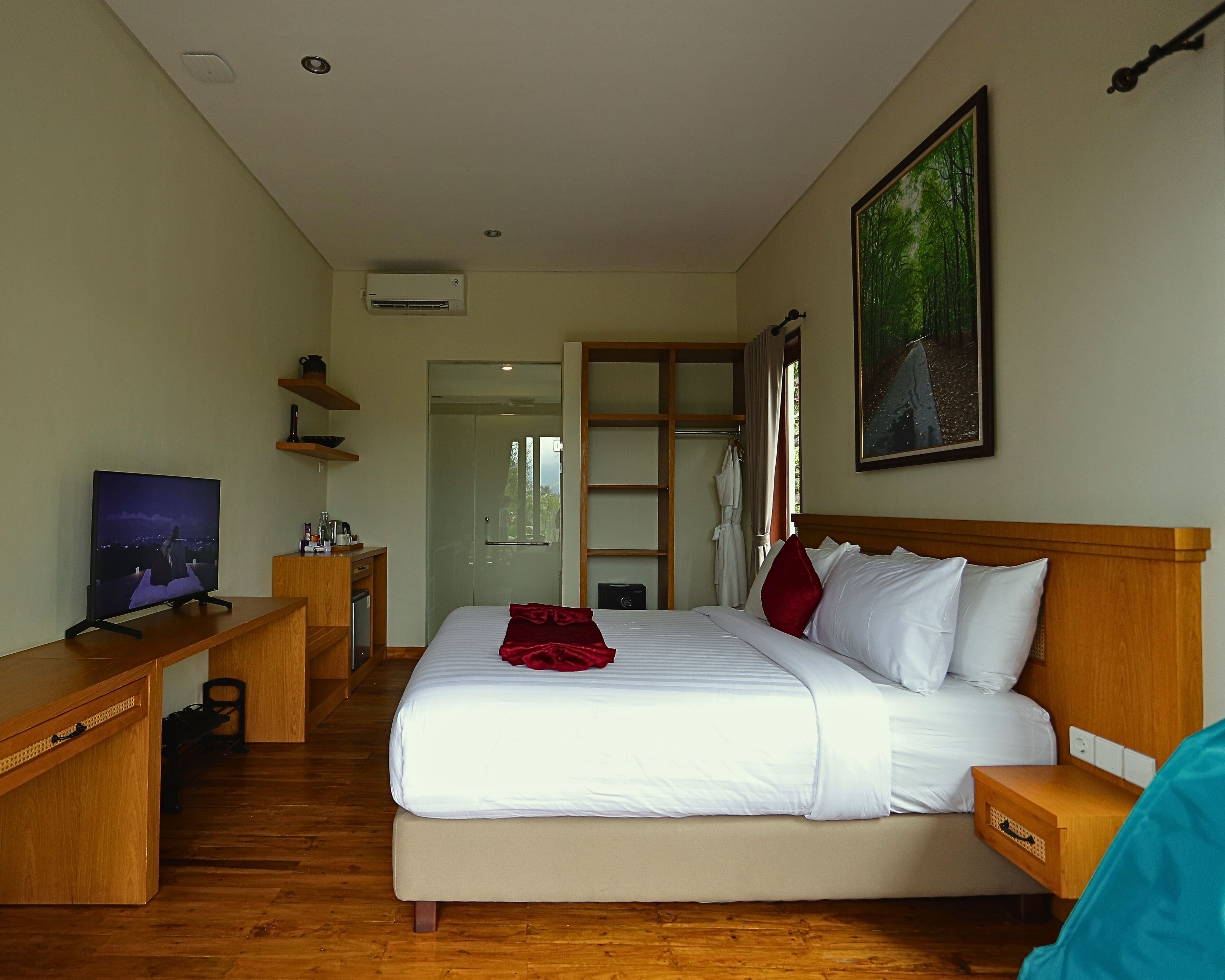 A hotel room with a bed, a desk, a TV, a painting, and a door leading to a bathroom.
