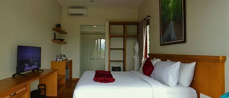 A hotel room with a bed, a desk, a TV, a painting, and a door leading to a bathroom.
