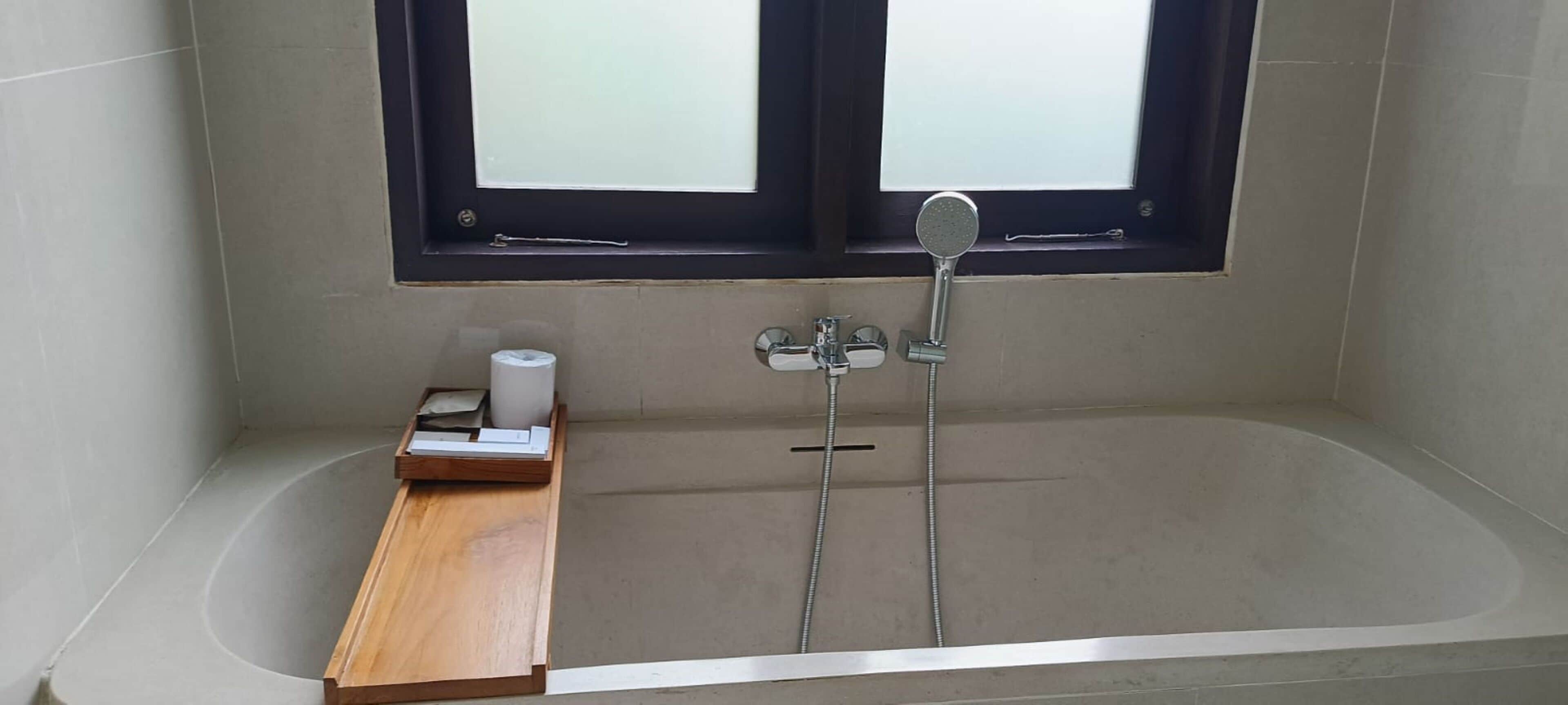 Un baño con bañera, ventana y una bandeja de madera con un rollo de papel higiénico.