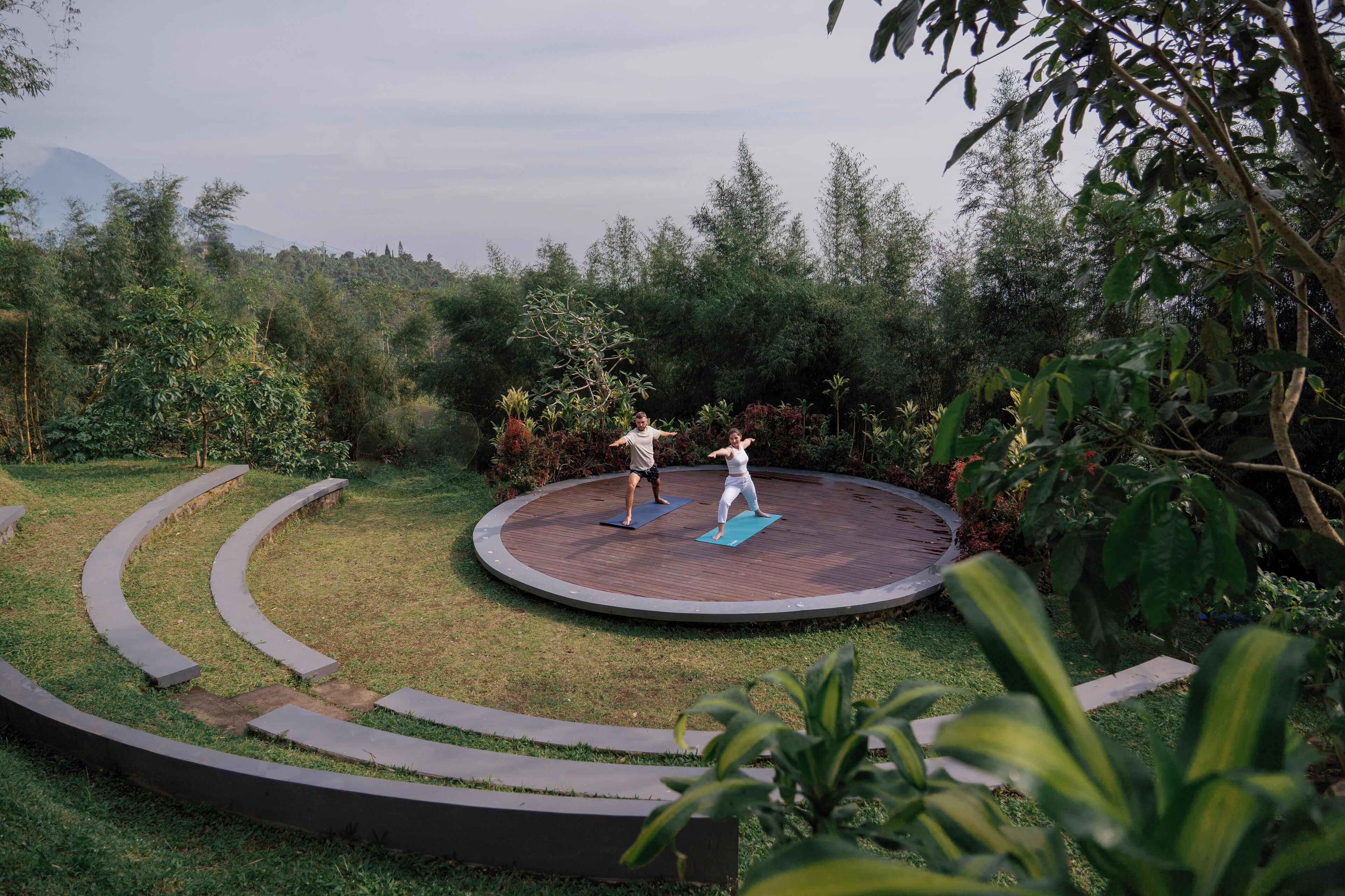 Un área de ejercicios al aire libre circular, rodeada de follaje, con dos personas practicando yoga.
