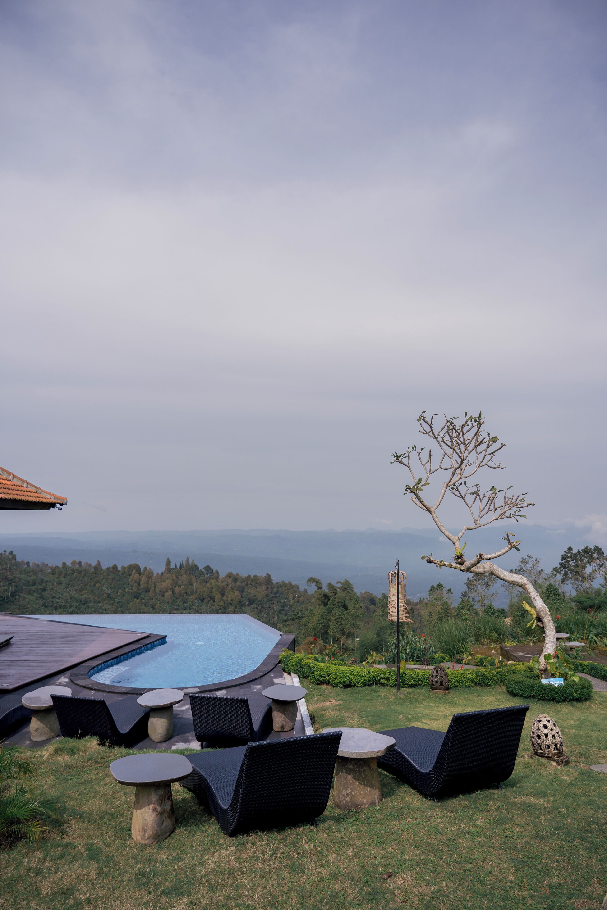 A pool area with lounge chairs and a hot tub, surrounded by a garden and a view of distant mountains.