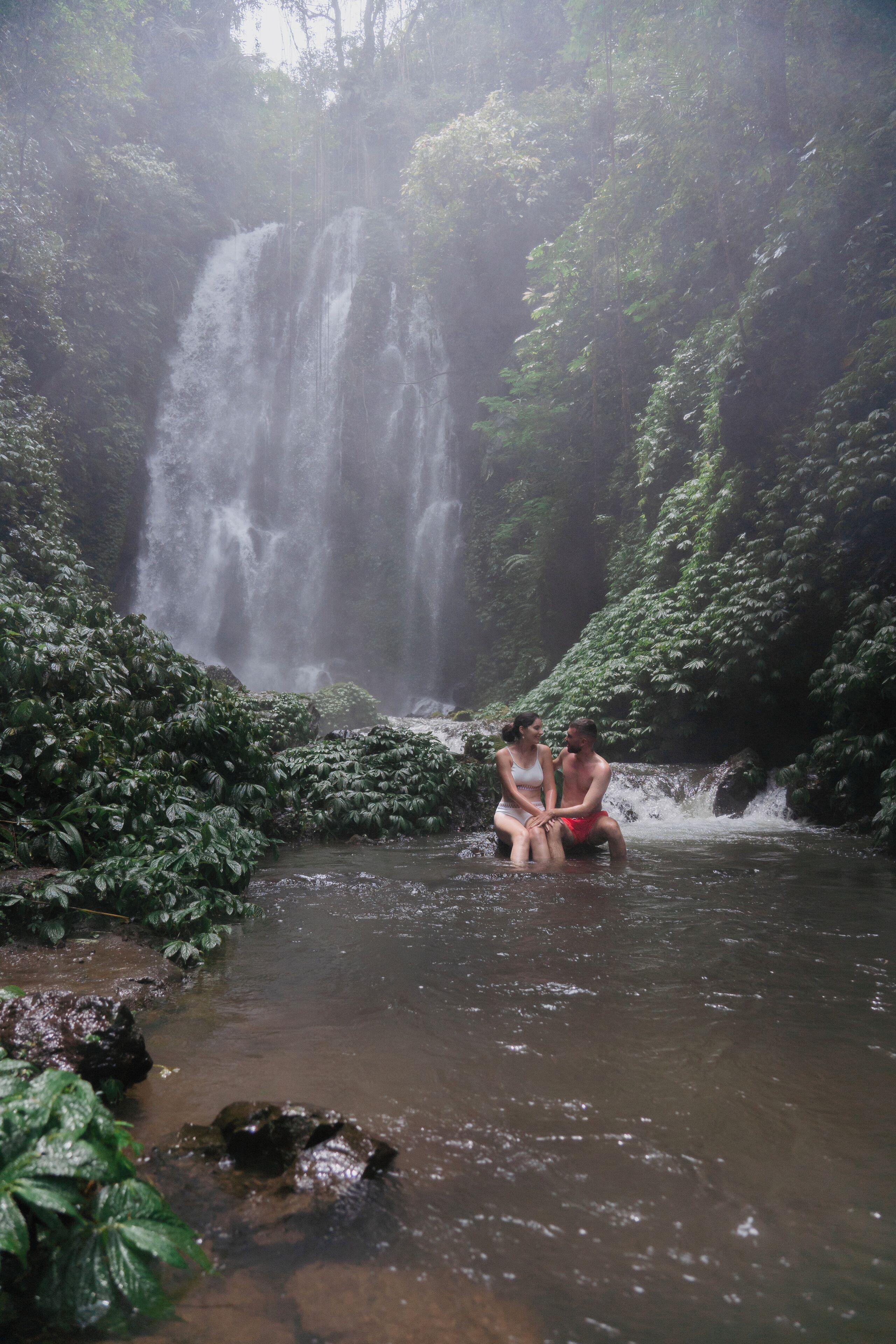 Un couple est assis près d’une cascade, dans un cadre verdoyant et luxuriant.