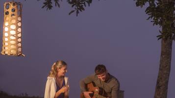 Two people sitting by a fire, one playing guitar, and a hanging lantern.