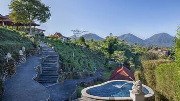 A traditional building with a red roof, a stone staircase leading up to a wooden deck, and a pool area with a statue.