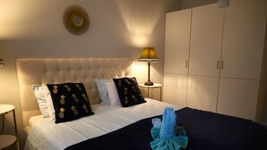 A hotel room with a tufted headboard, a bed with white linens, two black pillows with pineapple patterns, a blue towel, and a gold-framed mirror on the wall. - Brodderud Apartments (Mariestad)
