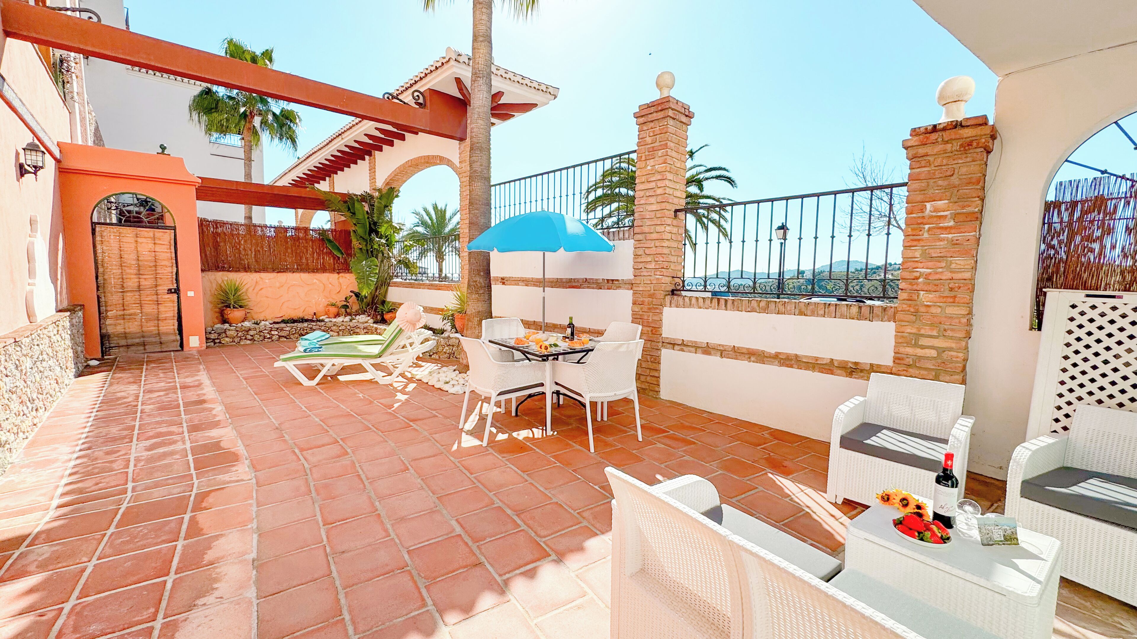 A patio with outdoor furniture, a blue umbrella, and a view of the sea.