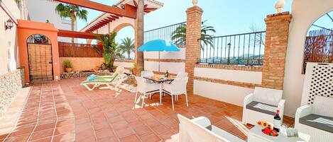 A patio with outdoor furniture, a blue umbrella, and a view of the sea.